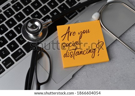 Selective focus of stethoscope, laptop, glasses and memo note written with question ARE YOU SOCIAL DISTANCING?. Health concept. 