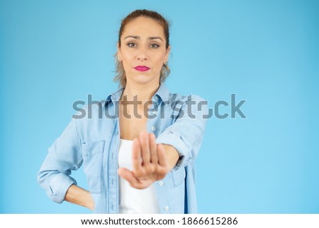 Portrait of a serious young woman standing with outstretched hand showing stop gesture isolated over blue background