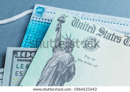 A US stimulus check on with some one-hundred-dollar bills and a medical mask Royalty-Free Stock Photo #1866625642