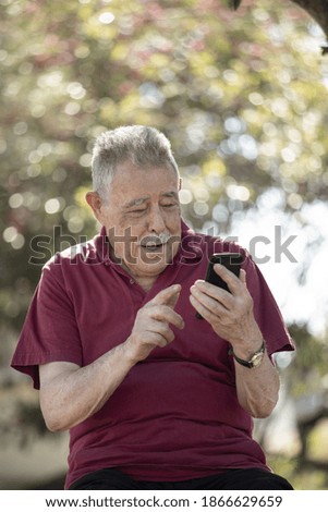 Smiling senior uses his own with his smartphone in an open air park