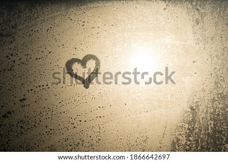 Close up hand drawing of a heart on a natural foggy window glass background. Valentine's day inspiration, close-up photo. An emotional sense of hope and love