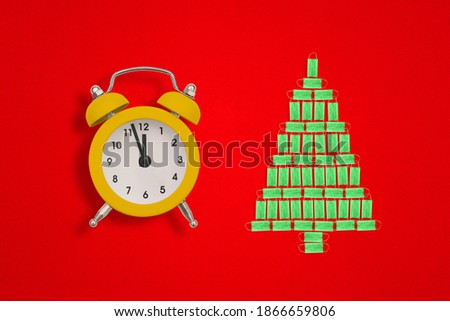 Christmas tree made of medical face masks and an alarm clock on a red background. The hands of the clock show twelve o'clock. Christmas idea