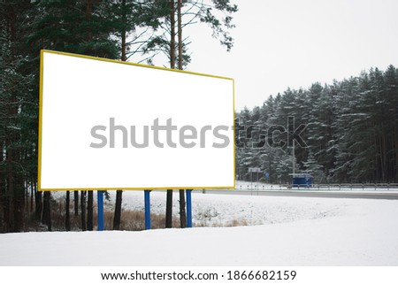 Billboard with white canvas by the road on the background of a winter forest