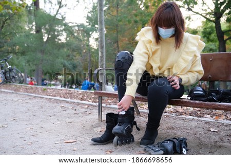 Young caucasian woman wearing face mask is wearing her roller skates in a park. Outdoor activities during the coronavirus pandemic.