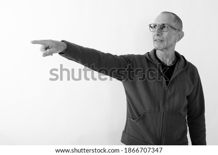 Studio shot of bald senior man pointing at distance while wearing eyeglasses against white background