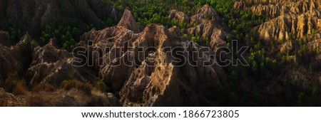 Panoramic view of amazing rock formations sculpted by rain and wind over a green pine forest at sunset