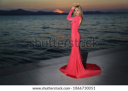 Blonde woman in a red dress on the beach enjoys the sunset