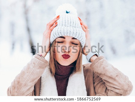 Close-up portrait of happy girl in woolen hat enjoying winter moments. Outdoor photo of laughing lady in knitted hat having fun in snowy morning on blur nature background.
