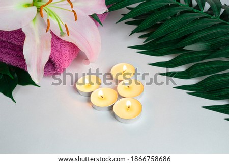 The concept of spa beauty treatments, lily flower, towel, tropical palm leaves, several candles on a white background. copy space