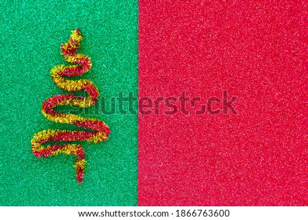 Red and yellow figurine of a Christmas tree on a shiny green - red background. Copy space.