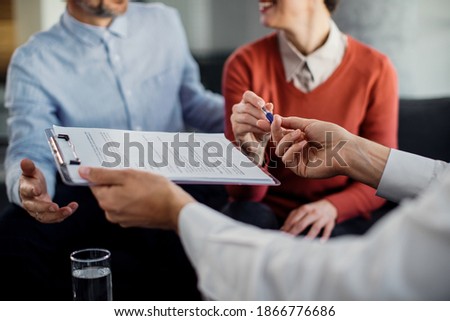 Close-up of woman signing an agreement with insurance agent while being on a meeting with her husband. 