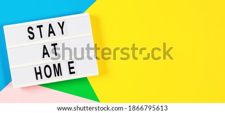 Lightbox with text STAY AT HOME on yellow, green, pink and light blue background. Top view