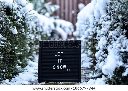 Black letter board with white letters "Let it snow", on the background of snowy winter doorway next to the house entrance door.