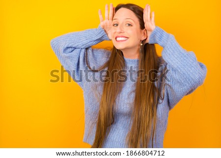Young beautiful Caucasian woman wearing knitted sweater against yellow background  Trying to hear both hands on ear gesture, curious for gossip. 