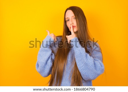 Young beautiful Caucasian woman wearing knitted sweater against yellow background  asking to be quiet with finger on lips pointing with hand to the side. Silence and secret concept.