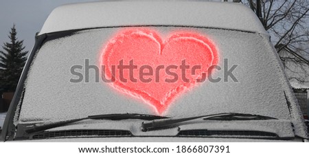 red Heart drawn on a car windshield covered with fresh Christmas snow.  Windscreen wipers and a snow covered car or bus.winter season. front view. happy Valentines day. 14th february
