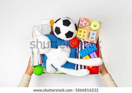 Donation concept. Volunteer hands holding donate box with clothes, books and toys on white background. Top view