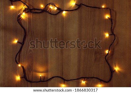 Frame of bright Christmas lights on wooden background, flat lay. Space for text