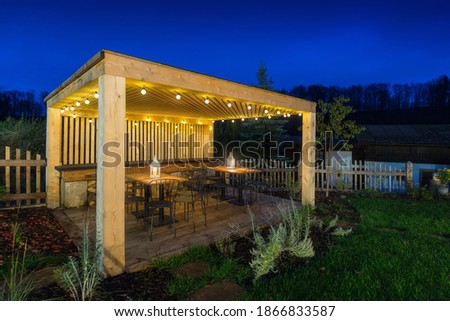 Gazebo with lights at night. Picture of a summer house with comfortable garden furniture. Romantic scene in dusk.