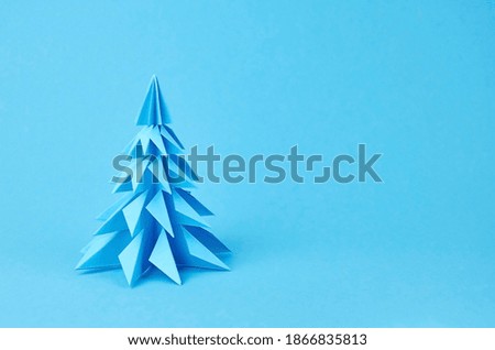 Paper origami christmas tree on blue background, winter holidays concept