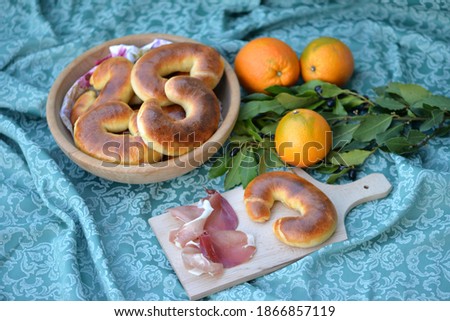 Home baked milk rolls with butter in wooden bowl and one bread bun with smoked ham on wooden board; soft bread buns with laurel and oranges in background