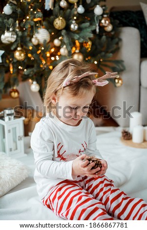 Christmas portrait of an adorable 2 year old girl dressed in festive pajamas near the Christmas tree. Winter vacation. New Year's Holidays.