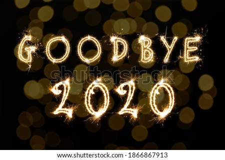 Goodbye 2020. Bright text made of sparkler on black background with blurred lights