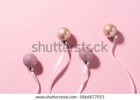 Creative composition with shining pink Christmas toy balls with ribbons on pink pastel background. Christmas and New Year concept.