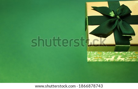 green gift box with gold cover and green ribbon bow, isolated on green background. Christmas picture