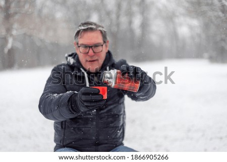 Man in a snow storm pouring a drink from a thermos