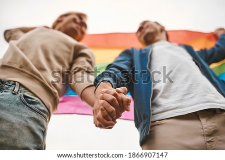 Romantic gay couple hugging, kissing and holding hands outdoors. Two handsome men holding LGBT pride flag. Royalty-Free Stock Photo #1866907147