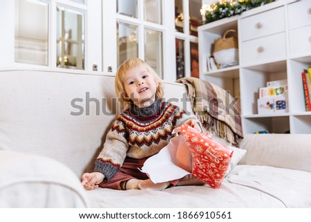 a little boy is sitting on the sofa at home in a cozy living room and unpacking a new year's gift