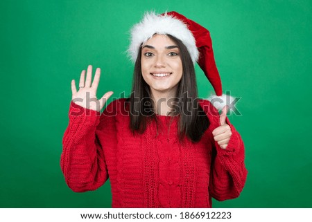 Young beautiful woman wearing Christmas Santa hat over isolated green background showing and pointing up with fingers number six while smiling confident and happy