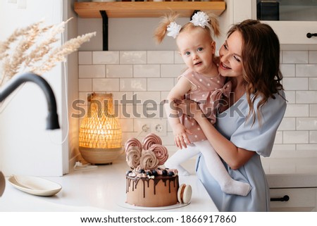beautiful woman holds in her arms a little girl near the birthday cake. portrait of mom and daughter in the kitchen