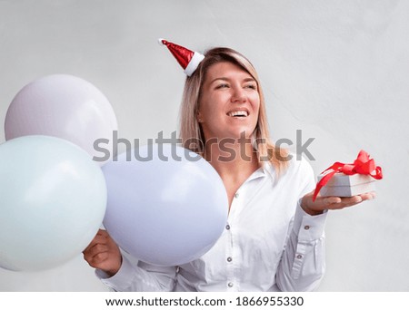 girl in Santa hat with a gift on a gray background. woman holding balloons and gift box