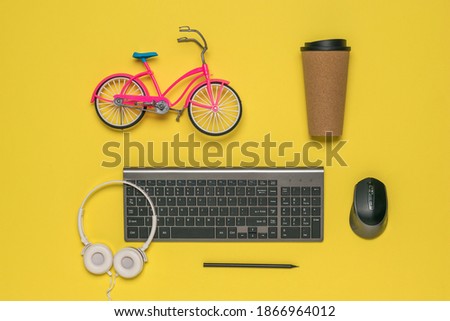 A small toy Bicycle, a glass of coffee and a wireless keyboard on a yellow background. Designer's workplace.