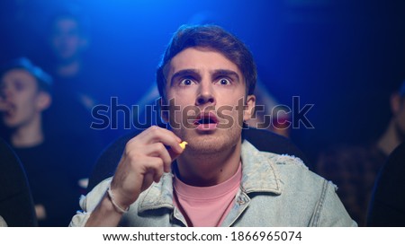 Focused man looking interesting film in dark hall. Portrait of surprised guy eating popcorn in movie theater. Closeup worried male person spending evening in cinema. Royalty-Free Stock Photo #1866965074