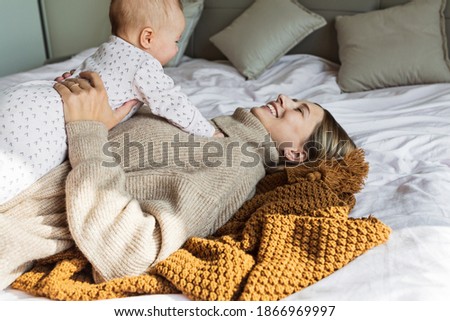 Cute caucasian baby girl lying on cozy bed with her mother dressed in knitted sweater brown color. Stay at home during Coronavirus covid-19 quarantine. concept of motherhood, childhood and health care