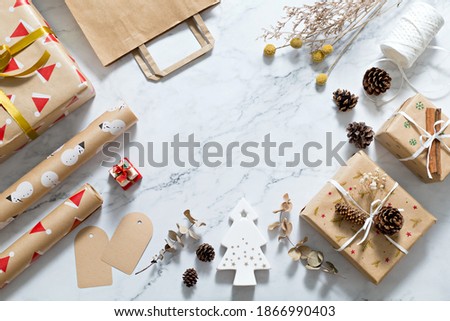 Christmas composition on white marble background with white christmas tree, gift box, ribbon, gift tag, wrapping paper and pine cone. Minimal, flat lay with copy space.