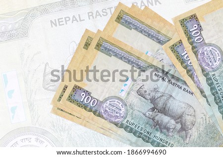 100 Nepalese rupees bills lies in stack on background of big semi-transparent banknote. Abstract presentation of national currency. Business concept