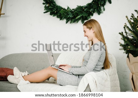 Young woman using laptop and working at home office near decorated pine tree with Christmas interior. Christmas sales. Girl typing on laptop in home. Xmas concept. Planning holidays. Web search.
