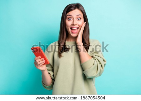 Photo portrait of impressed woman touching cheek face holding phone in one hand isolated on vivid cyan colored background