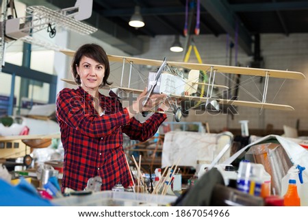 Portrait of smiling woman with biplane model having fun in aircraft workshop