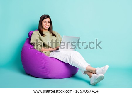 Photo portrait full body view of girl working on laptop sitting in purple beanbag armchair isolated on vivid teal colored background
