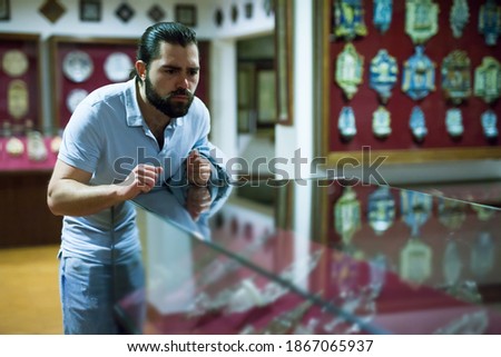 Attentive adult man exploring artworks in glass case in museum. High quality photo