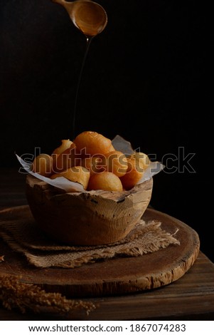 selective focus of traditional Greek doughnuts called loukoumades in a wooden bowl against dark background