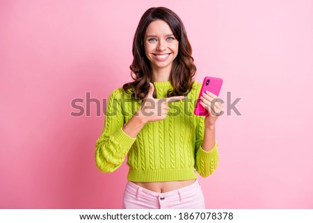 Photo of funny cheerful girl hold phone indicate finger offer wear green sweater isolated pink color background