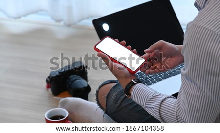 Cropped shot of photographer or designer is sitting on the floor in front of his laptop and using smart phone.