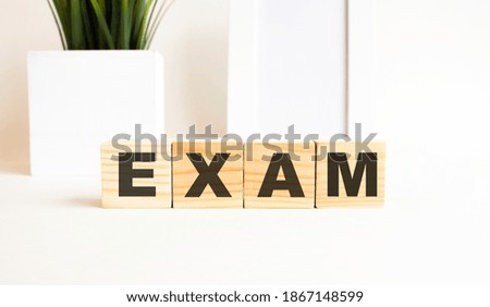 Wooden cubes with letters on a white table. The word is EXAM. White background.