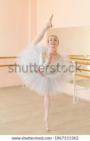 Beautiful ballerina in body and white tutu is training in a dance class. Young flexible dancer posing in pointe shoes.